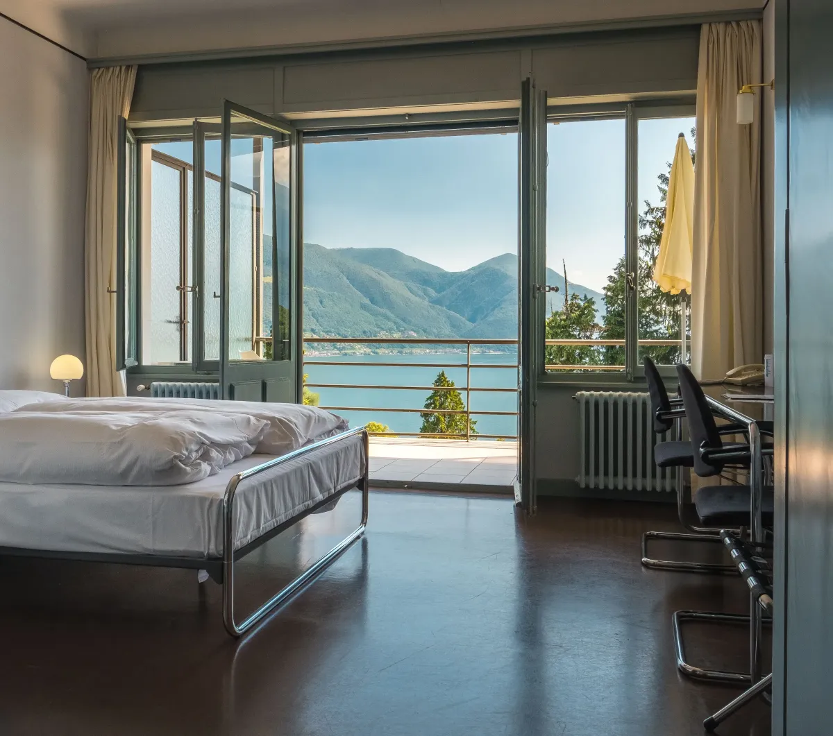 A guest room at Monte Verità, its balcony doors open onto Lago Maggiore and the mountains